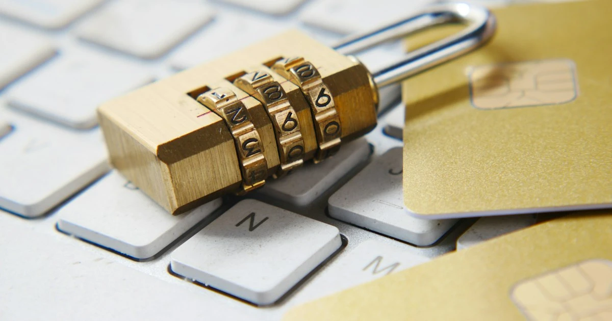 Brass combination padlock resting on a white laptop keyboard next to bank cards