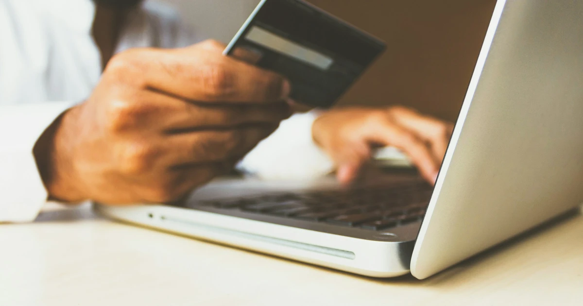 Hand holding a credit card next to a laptop while typing, ready to manage an online payment