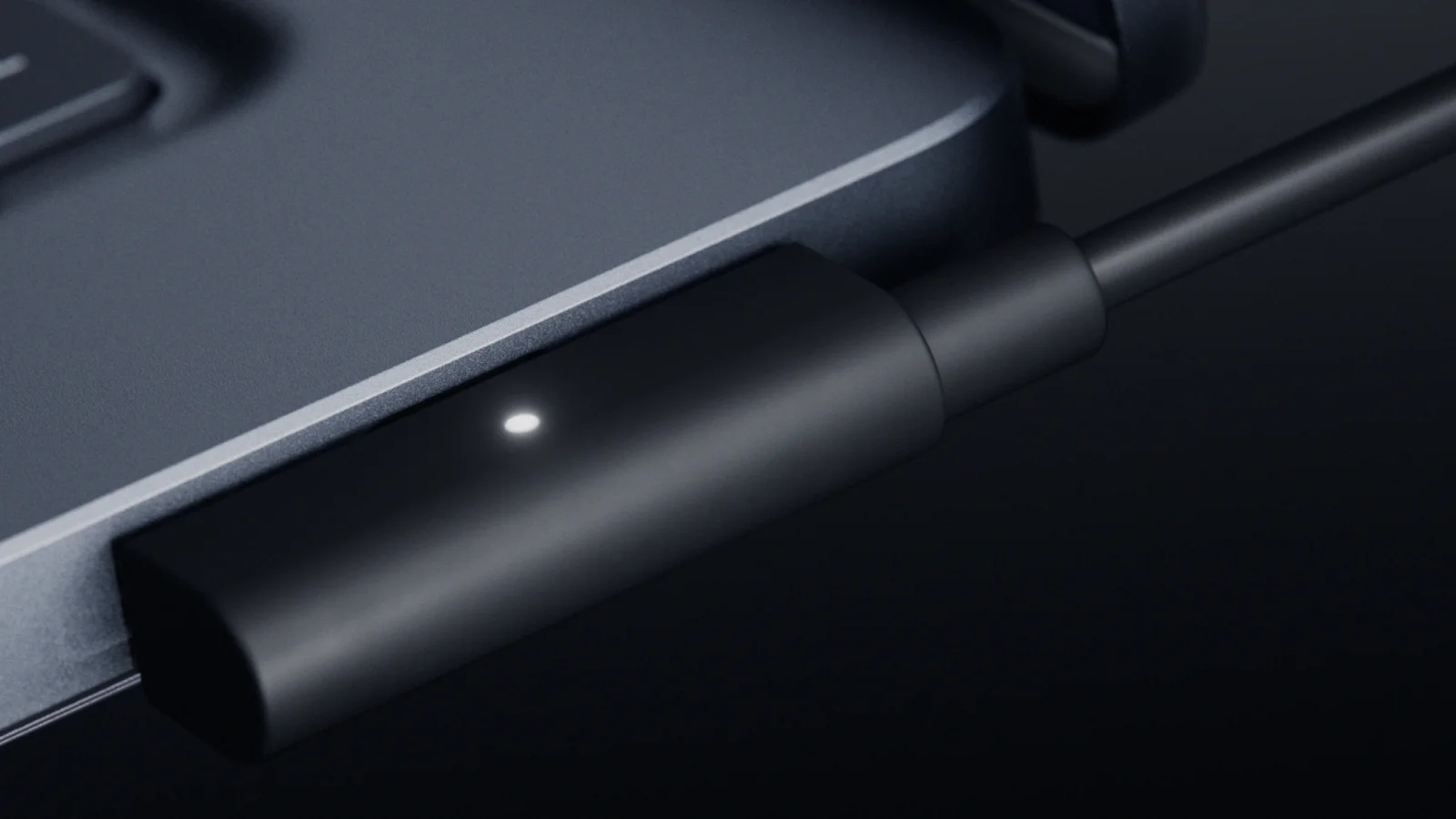 Close-up of the magnetic USB-C charging cable attached to the side of Surface Laptop Ultra, with a small status light on the connector